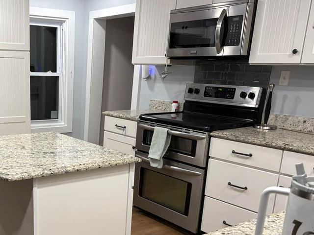 Kitchen with an island, white cabinets, granite countertops and electric range
